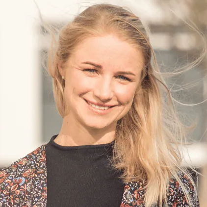 Bright young woman smiling outdoors with wind blowing her hair, wearing a patterned jacket and black top, reflecting positive energy and confidence for digital messaging services.